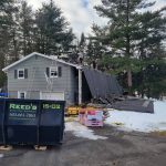 Workers removing the shingles off of a house's roof with a Reed's dumpster on site