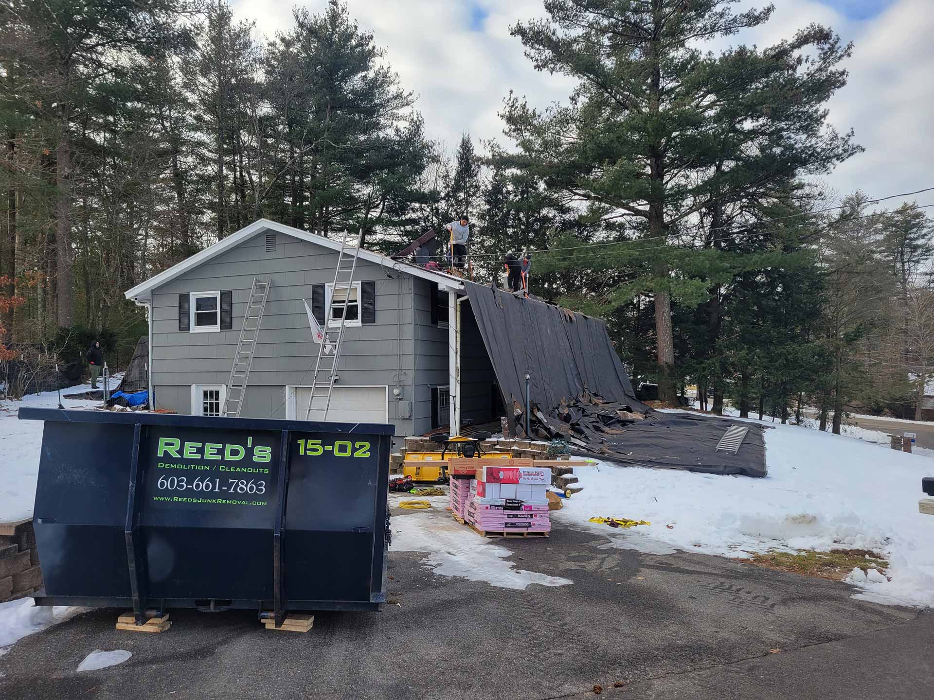 Workers removing the shingles off of a house's roof with a Reed's dumpster on site